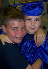 ben graduating from preschool in his cap and gown, being hugged by his brother